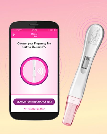 Tela de celular com o aplicativo de teste de gravidez no celular ao lado de um teste de farmácia